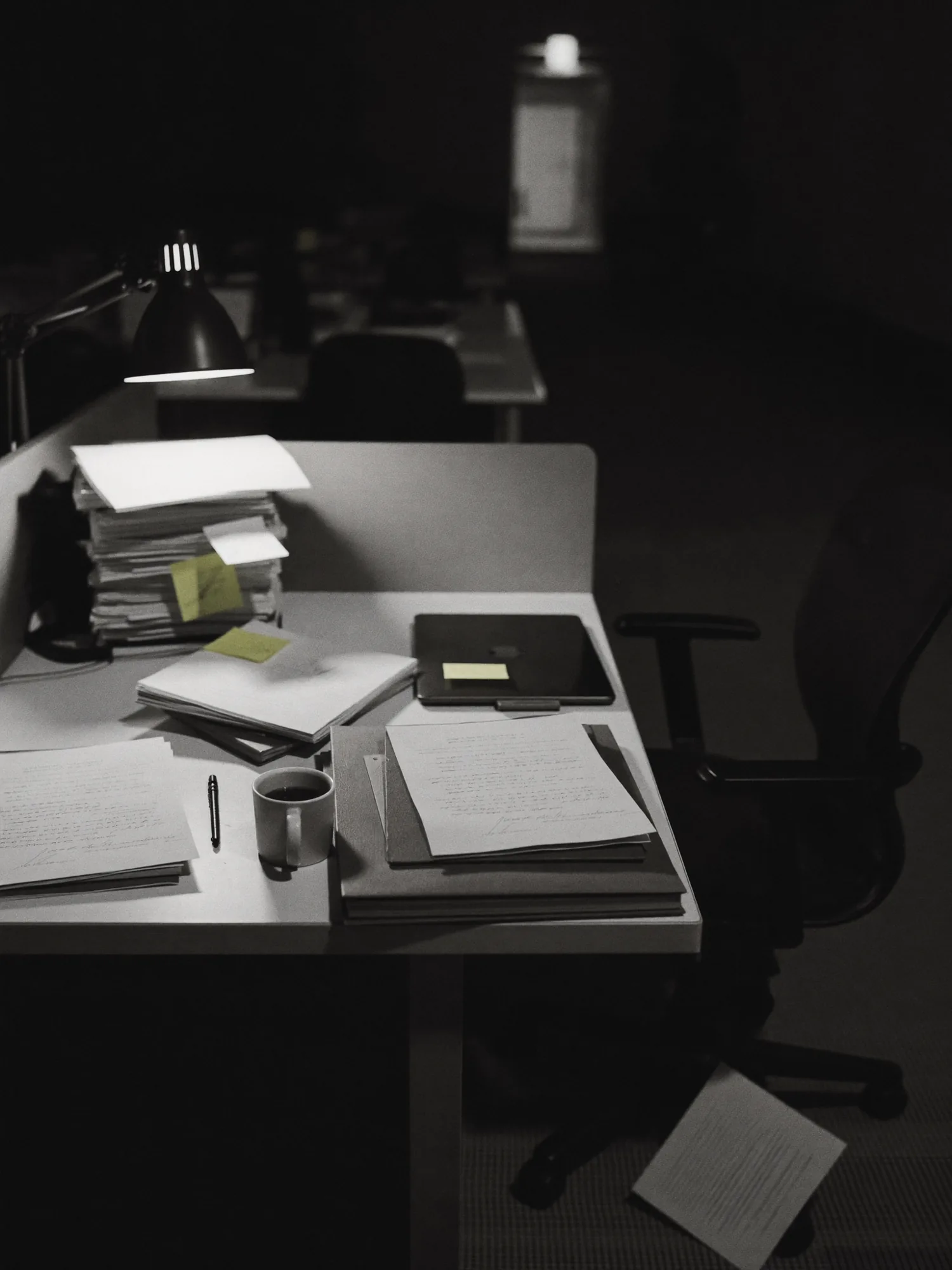 Desk at night, CVs piled high, lamp on, chair empty